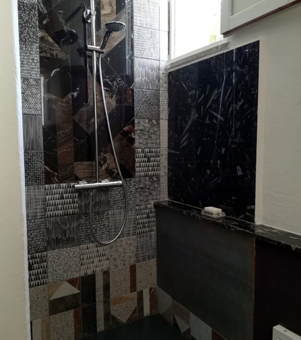 Une salle de bain avec douche, murs carrelés et comptoir en marbre.