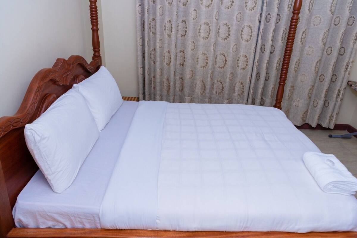 A neatly made bed with a wooden headboard, white bedding, and a folded towel on the side.