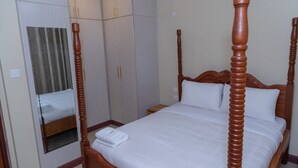 A four-poster bed with a wooden headboard, a mirror, and a wardrobe with two doors. - Stay.Plus Airport Transit House (Syokimau)