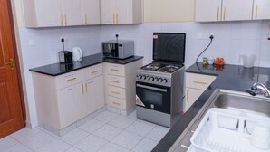 A compact kitchen with a gas stove, microwave, toaster, and cabinets. - Stay.Plus Airport Transit House (Syokimau)