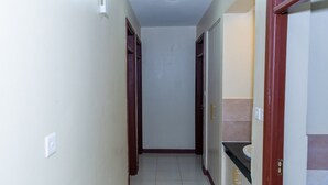 A narrow hallway with a tiled floor, wooden doors, and a light switch on the wall. - Stay.Plus Airport Transit House (Syokimau)