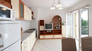 A kitchen with a microwave, stove, and cabinets. There is a television on a wooden stand and a dining table with chairs. - Modern apartment in Dramalj near the sea (Dramalj)