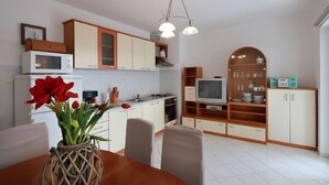 A modern kitchen with white cabinets, a microwave, a stove, and a dining area with a table and chairs. - Modern apartment in Dramalj near the sea (Dramalj)