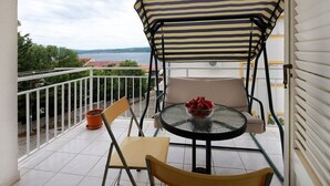 A balcony with a striped awning, a round glass table with a bowl of fruit, and a chair. - Modern apartment in Dramalj near the sea (Dramalj)