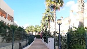 A pathway lined with palm trees and a fence, leading to a building with a white facade and balconies. - Belvilla by OYO Cala I (Vera Playa)