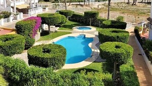 A pool area with two swimming pools, surrounded by well-manicured hedges and a white building with balconies. - Belvilla by OYO Cala I (Vera Playa)