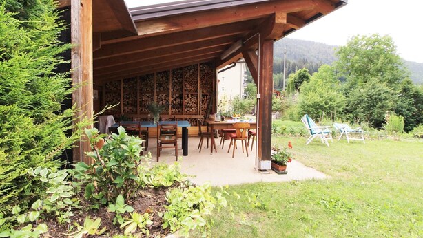 A wooden building with a covered patio area, outdoor seating, and a view of a mountainous landscape.