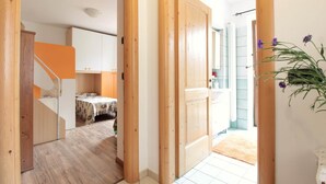A hallway with wooden doors leading to a room with a bed and a table.