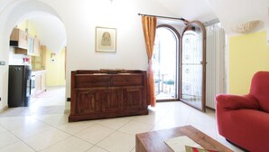 A living room with a wooden cabinet, a red sofa, and a kitchen visible through an archway.
