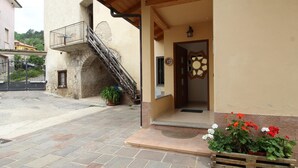 A building with a stone staircase leading to a balcony, a wooden door with a decorative glass panel, and a planter with flowers in front.