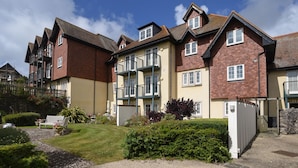 A residential building with multiple balconies, a garden area with a gravel path, and a potted lavender plant.