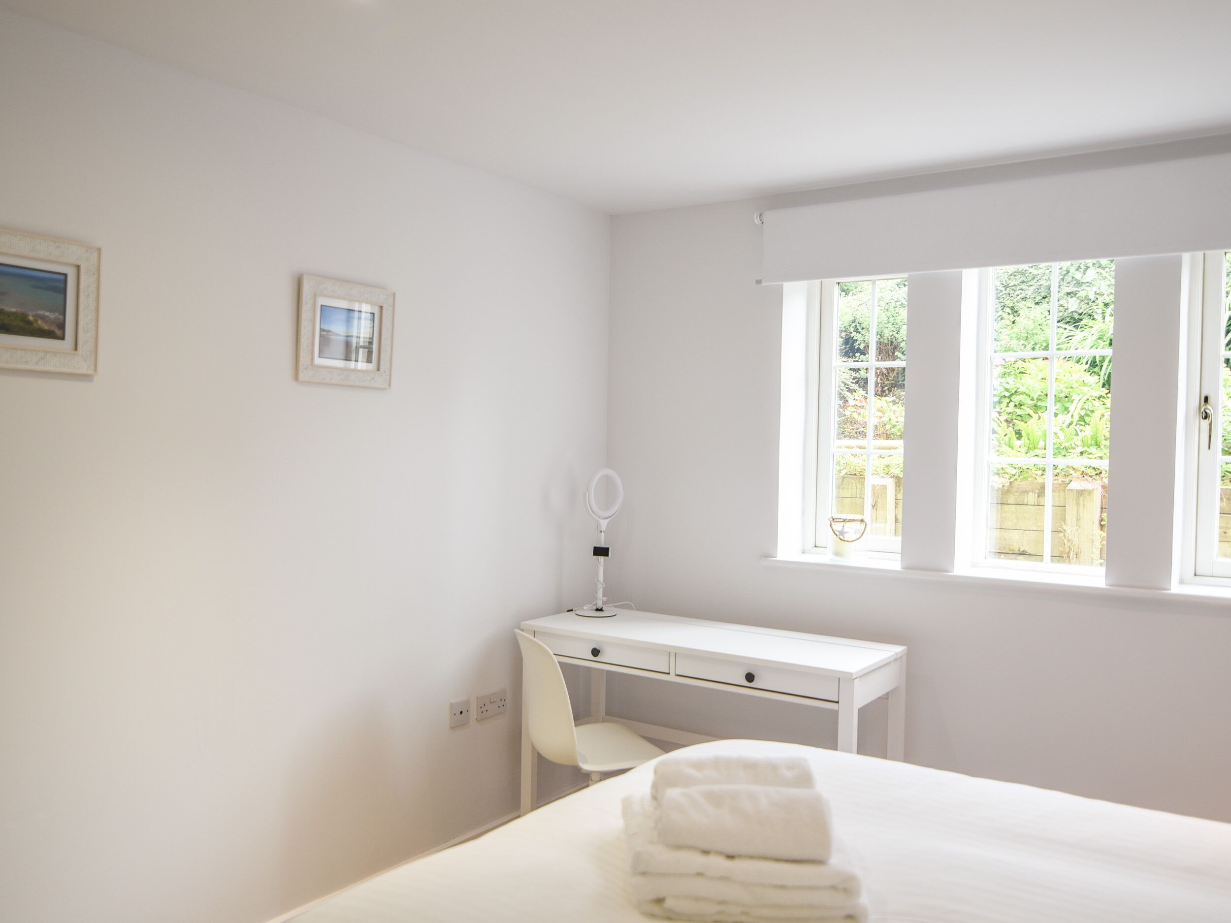 A clean, white room with a bed, a desk, and a window.