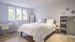 A bedroom with a bed, a desk, a chair, a wardrobe, and a window with a view of greenery.