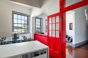 Una cocina moderna con una mesa de comedor de vidrio y una puerta roja que da a una zona de estar con un sofá rojo.