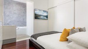 Een moderne slaapkamer met een bed, kussens, een schilderij en uitzicht op een badkamer.