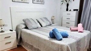 A bedroom with a bed, pillows, a nightstand, a dresser, and a lamp.