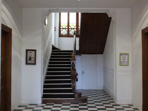 Uma escadaria com piso xadrez, corrimão de madeira e uma porta no topo.