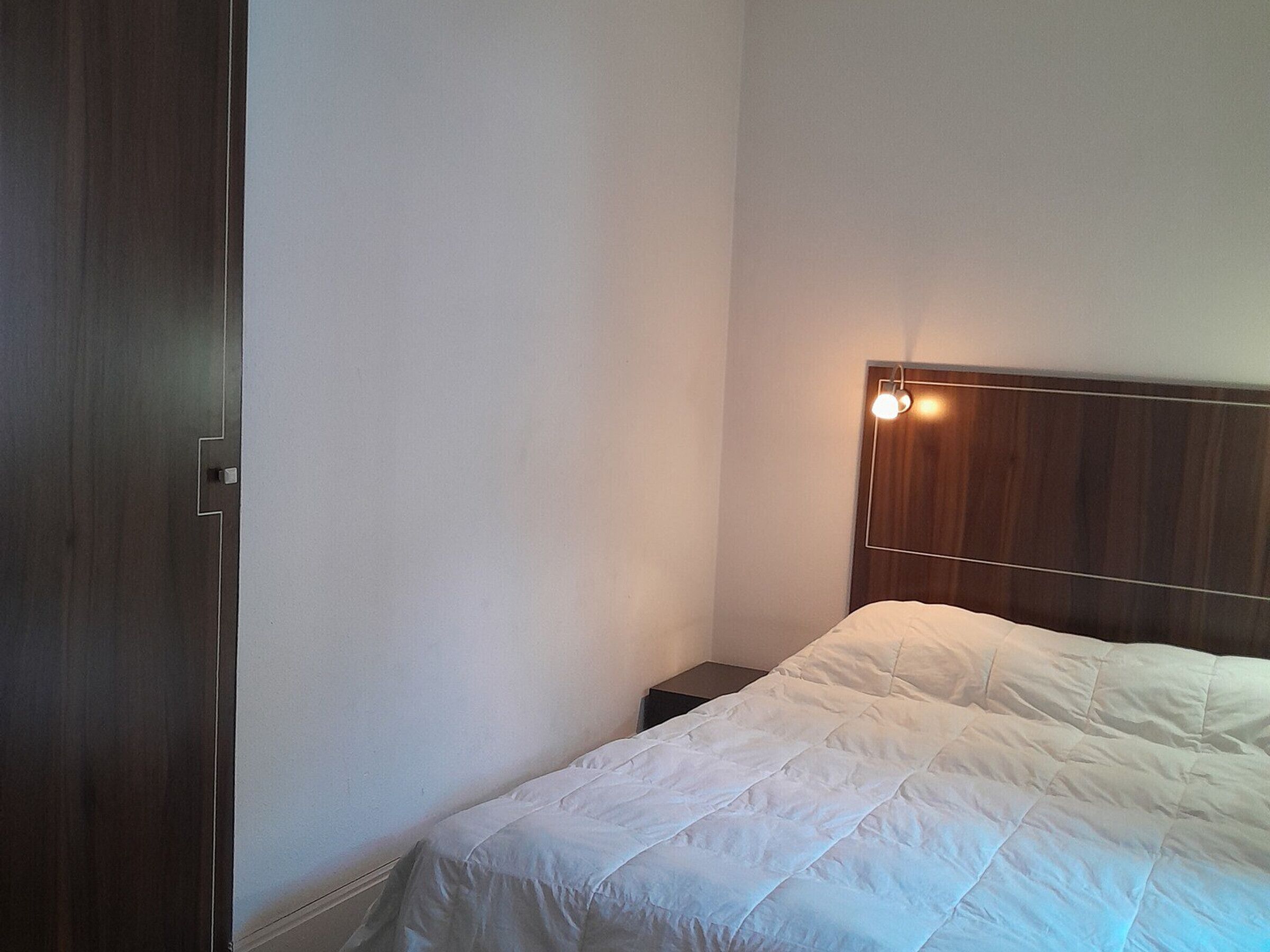 A bedroom with a wooden headboard, a white bedspread, and a small bedside table.