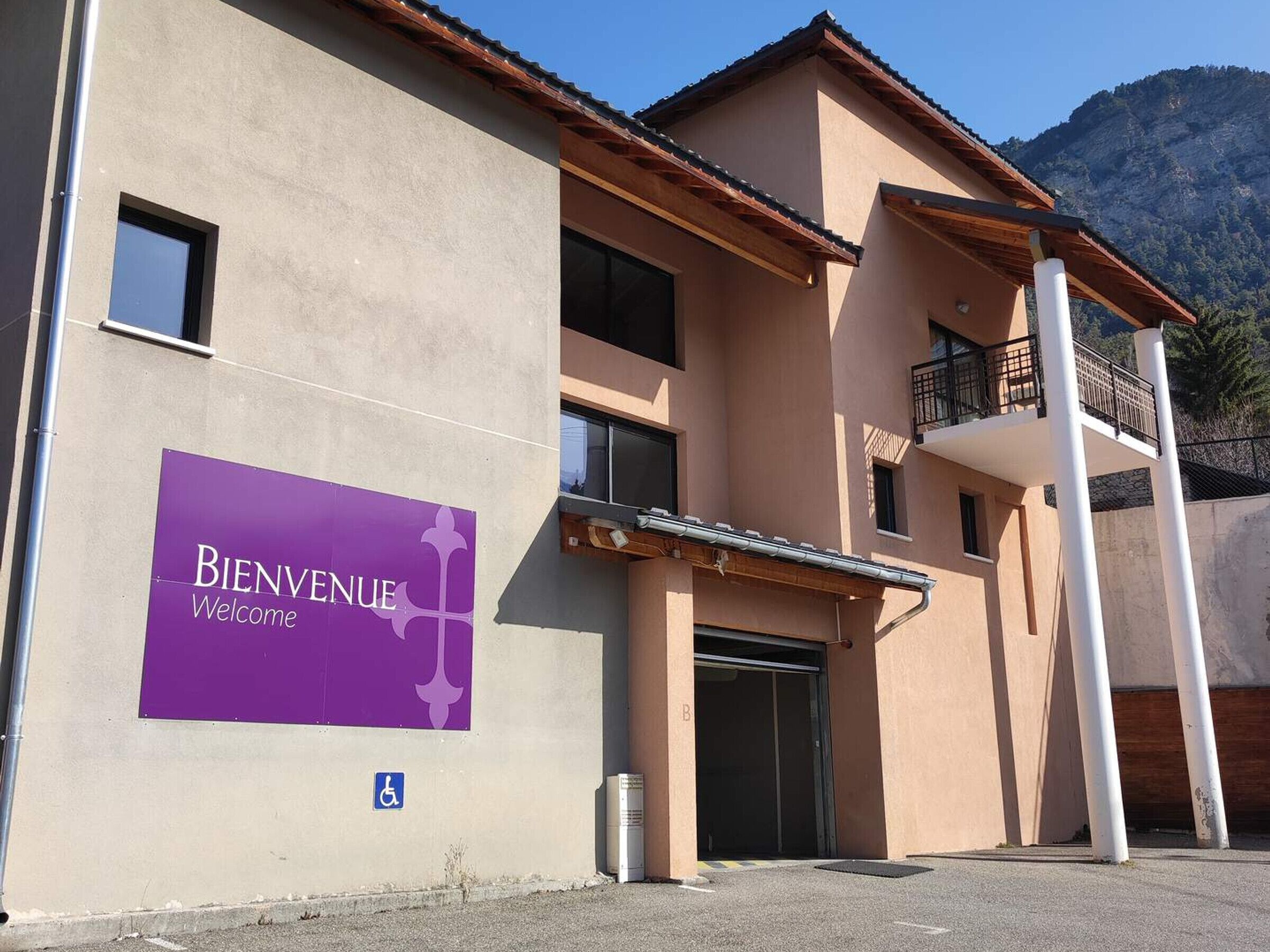 A building with a "BIENVENUE Welcome" sign, a wheelchair accessibility symbol, and a balcony.