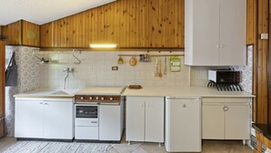 A compact kitchen with wooden paneling, a sink, a stove, a refrigerator, and a microwave. - Inviting apartment in Jadranovo with balcony/terrace (Jadranovo)