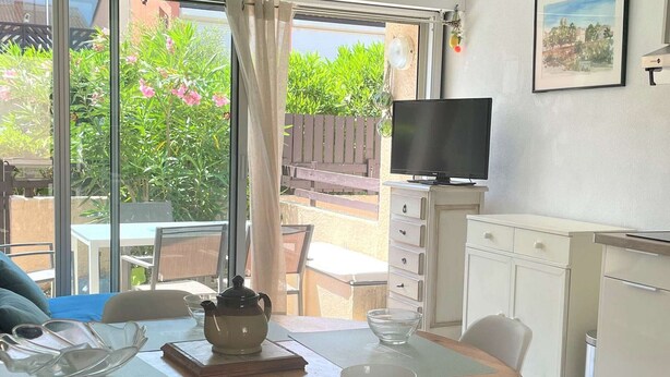 Ein Essbereich mit Holztisch, Stühlen, einem Fernseher und Blick auf den Garten durch große Fenster.