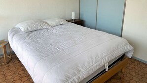 Ein Einzelbett mit weißer Daunendecke in einem Zimmer mit Fliesenboden und schlichter Wand.