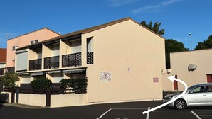 Ein Gebäude mit einer beigen Fassade, einem Balkon mit schwarzem Gitterwerk und einem Parkplatz mit einem Auto.