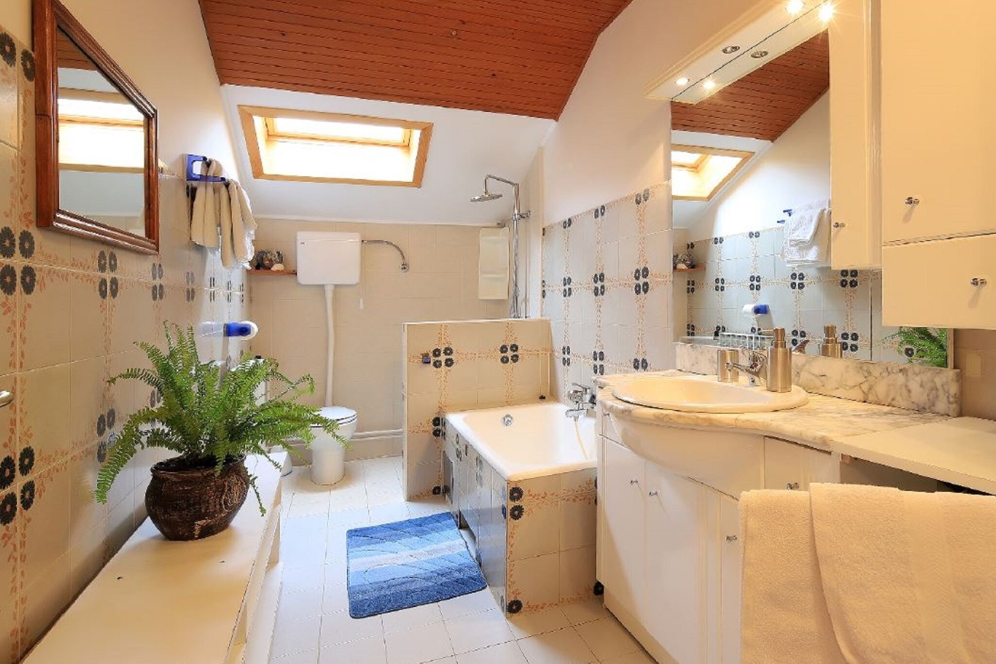 A bathroom with a bathtub, a sink, and a shower. There is a potted plant and a towel rack.