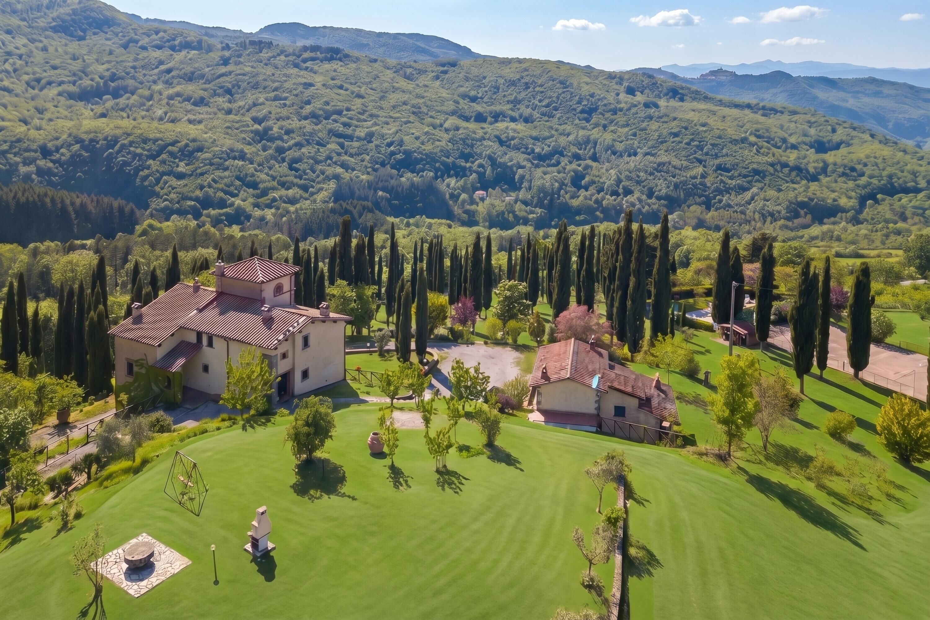 A large estate with multiple buildings, a well-maintained lawn, and a mountainous backdrop.