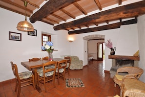 A dining area with a wooden table and chairs, a hanging light fixture, and a fireplace.