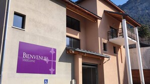 Un edificio con un cartel de 'Bienvenue Welcome', un símbolo de accesibilidad para sillas de ruedas y un balcón.