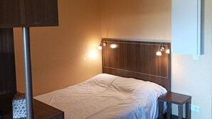 A modern hotel room with a wooden headboard, a single bed, a bedside table, and a nightstand.