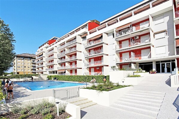 A multi-story hotel with a swimming pool, balconies, and a landscaped garden area.