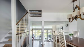 A spacious dining area with a wooden table and white chairs, a staircase with a wooden railing, and a chandelier. - Lovely Beach house in Amelia for 8 (Fernandina Beach)