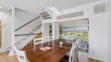 A spacious dining area with a wooden table, white chairs, and a view of the beach through large windows.