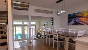 A dining area with a wooden table and white chairs, a staircase, and a view of the outdoors. - Lovely Beach house in Amelia for 8 (Fernandina Beach)