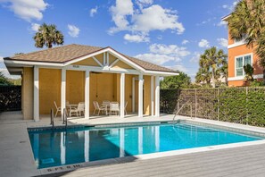 A swimming pool with a covered patio area, outdoor seating, and a fenced yard.