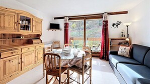 Ein gemütliches Wohnzimmer mit Esstisch, Holzschränken, einer Couch und einem Fernseher.