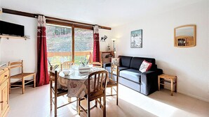 Ein gemütliches Wohnzimmer mit Esstisch, Stühlen, einer Couch und einem kleinen Holzschemel.