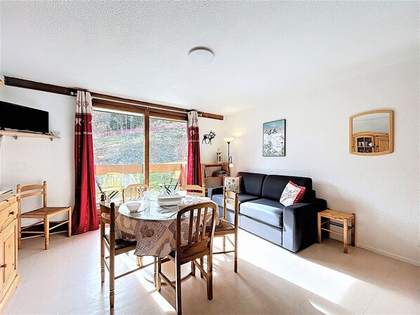 A cozy living room with a dining table, chairs, a sofa, and a small wooden stool.