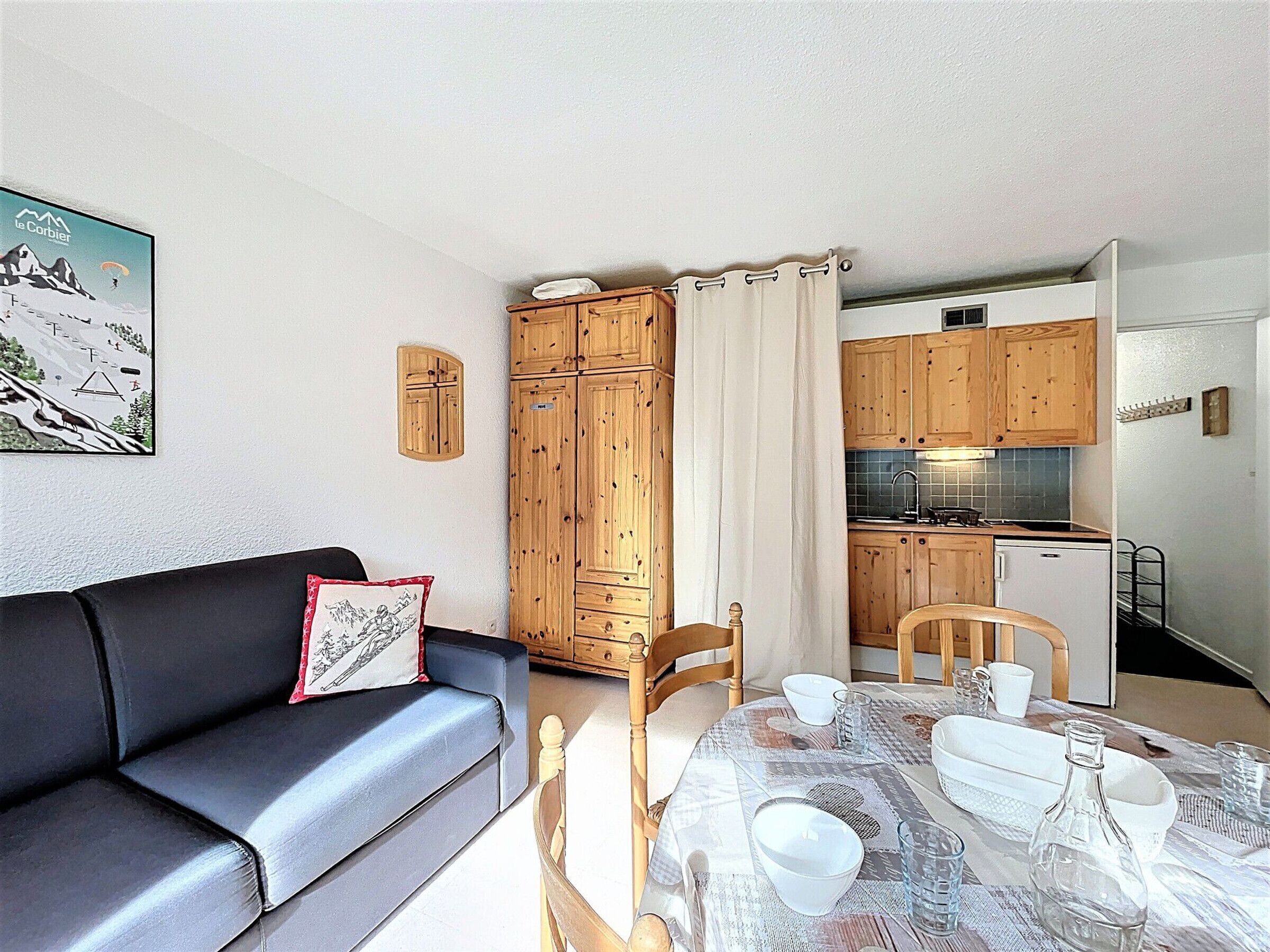 A living room with a black sofa, a dining table set with white dishes, and wooden cabinets.