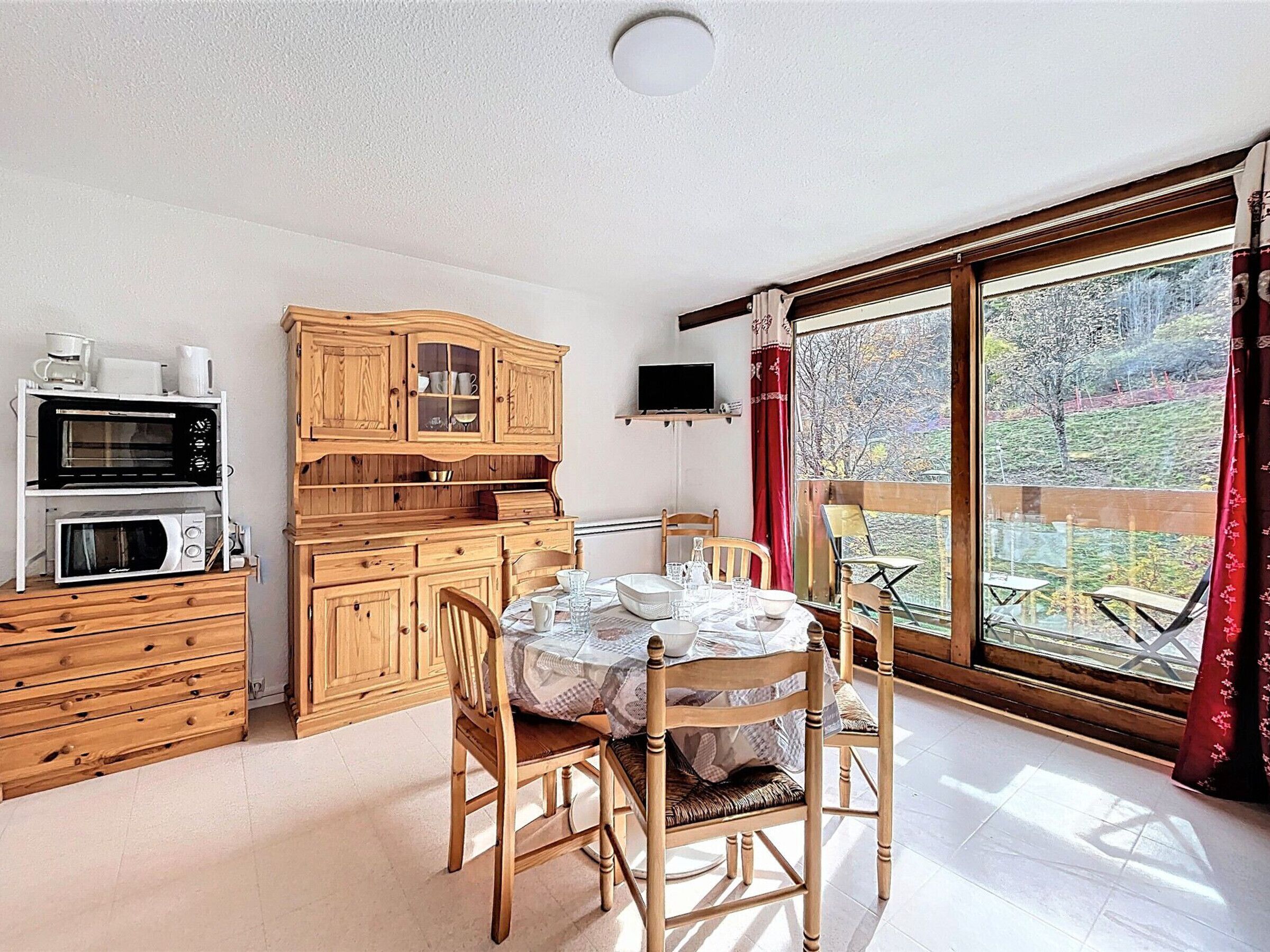 A dining area with a table set for four, wooden cabinets, a microwave, and a television on a shelf.