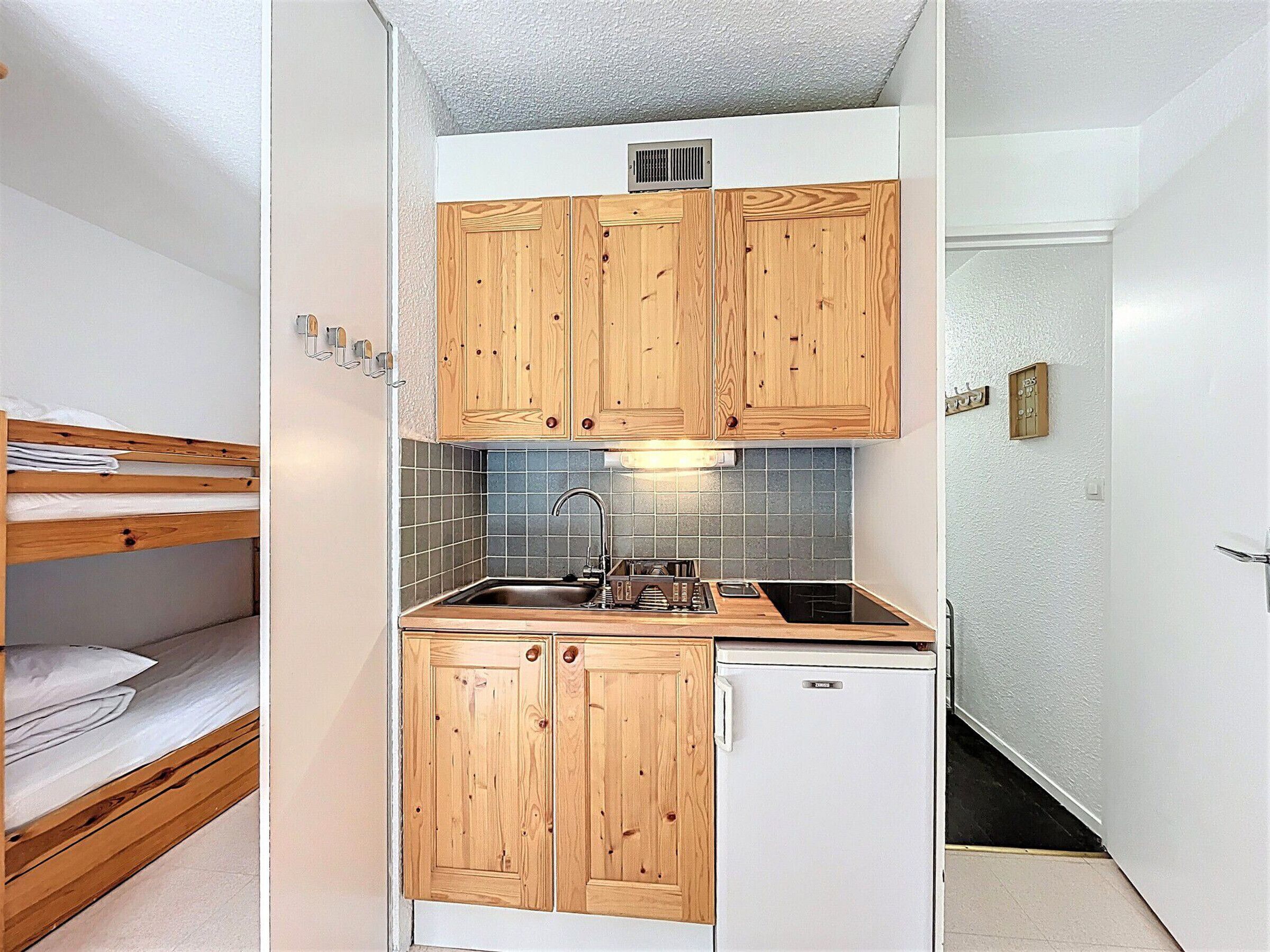 A compact kitchenette with wooden cabinets, a sink, and a small refrigerator.
