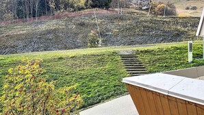 Blick vom Balkon auf einen angelegten Garten mit einer Holzterrasse und einem Steinweg, der einen Hügel hinaufführt.