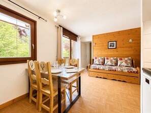 A room with a wooden dining table, chairs, a sofa, and a view of greenery outside. - Pleasant ski-in/ski-out apartment with pool (Flumet)