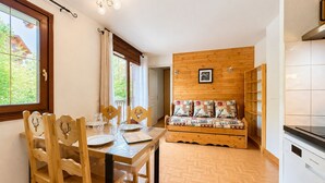 A dining area with a wooden table and chairs, a sofa with patterned cushions, and a view of greenery outside. - Pleasant ski-in/ski-out apartment with pool (Flumet)
