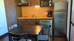 A compact kitchen with a wooden table, two chairs, a microwave, a coffee maker, and a dishwasher. - Studio for 4 pers with south terrace, pets allowed (Jausiers)