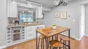 A modern kitchen with white cabinetry, a wooden table, and bar stools. - Modern Family Haven • Fenced Yrd • Grill/Firepit (Westminister)