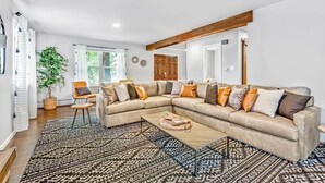 A spacious living room with a large L-shaped sectional sofa, a patterned rug, and a wooden ceiling beam. - Modern Family Haven • Fenced Yrd • Grill/Firepit (Westminister)