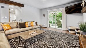 A modern living room with a sofa, coffee table, patterned rug, and a sliding glass door leading to an outdoor area. - Modern Family Haven • Fenced Yrd • Grill/Firepit (Westminister)